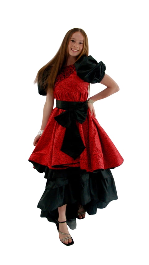 Young girl smiling in a red and black dress with large black bow detail, standing against white background