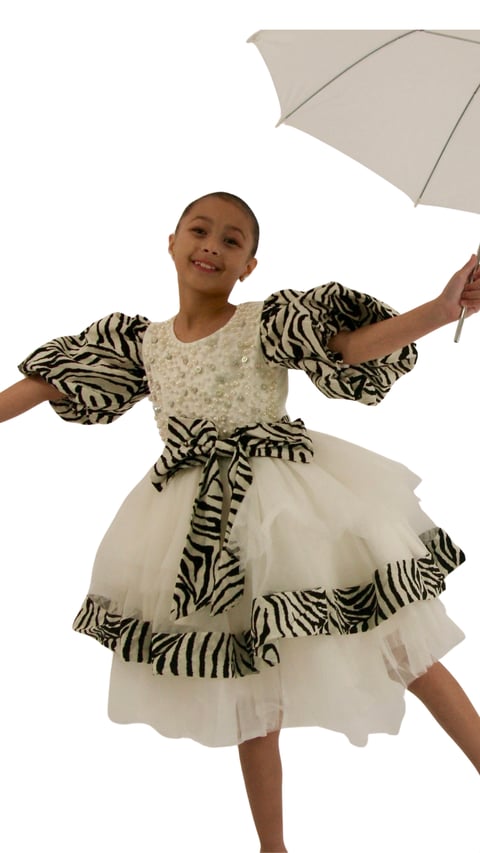 Young girl in zebra-striped and ivory dress holding an umbrella, smiling at camera against white background