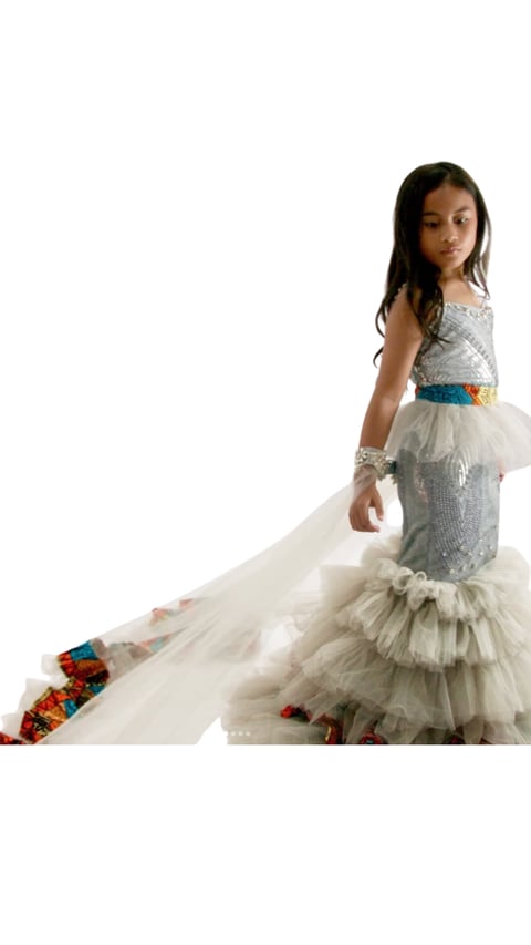 Young girl in a silver sequin and tulle mermaid-style dress with a blue belt, posing against a white background