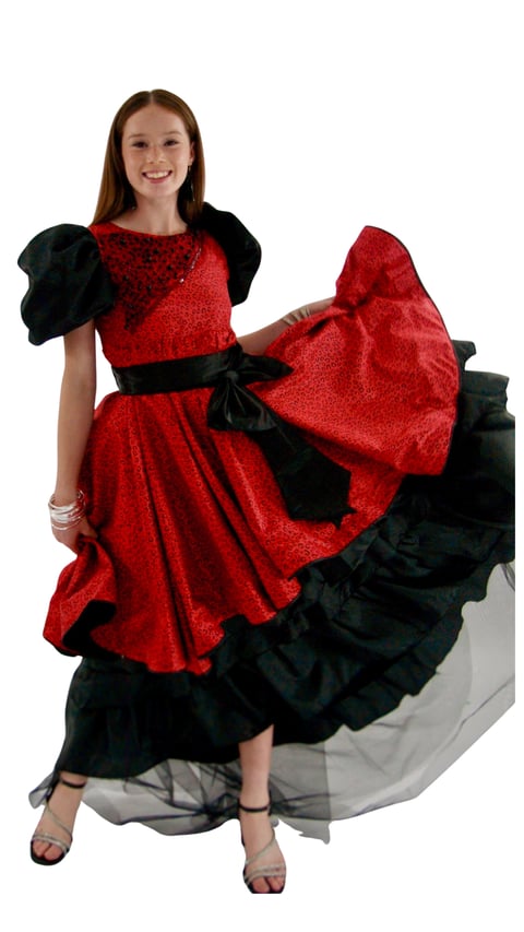 Young girl in a red and black sparkly dress with puffed sleeves and a large bow, posing with a smile against a white background