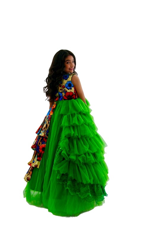 Young girl wearing a vibrant green tulle ball gown with colorful patterned top, posed looking over shoulder against white background
