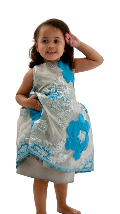 Young girl smiling at camera wearing a sleeveless blue and white floral dress with hand in hair