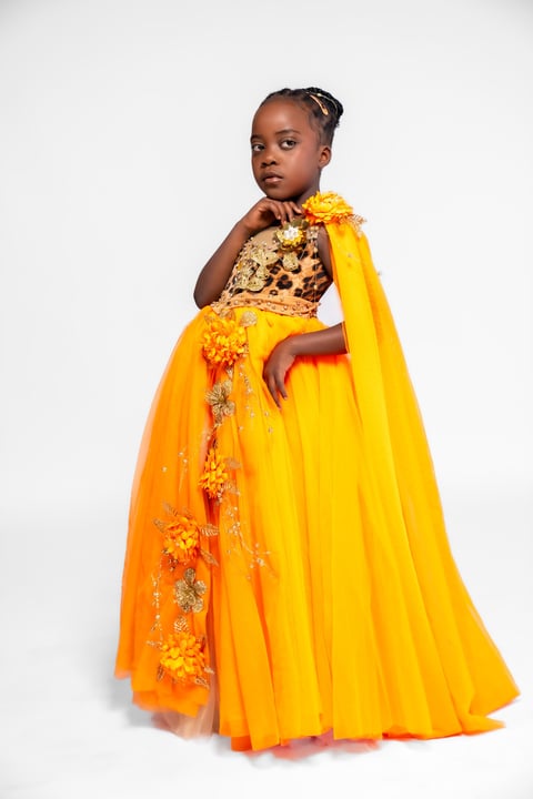Young girl in vibrant yellow and orange ceremonial dress with gold embroidered bodice and flowing cape against white background