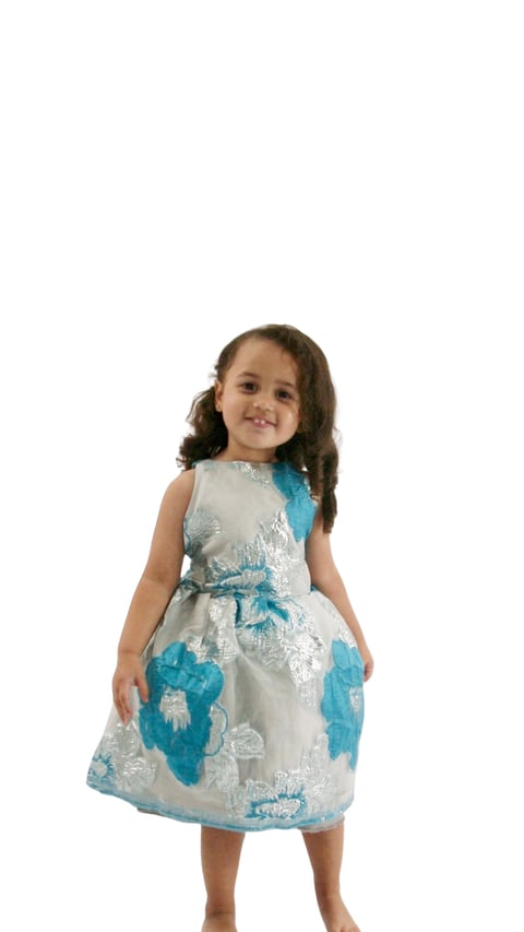 Young child wearing a white and blue sleeveless dress with floral pattern and bow belt, smiling at camera against white background
