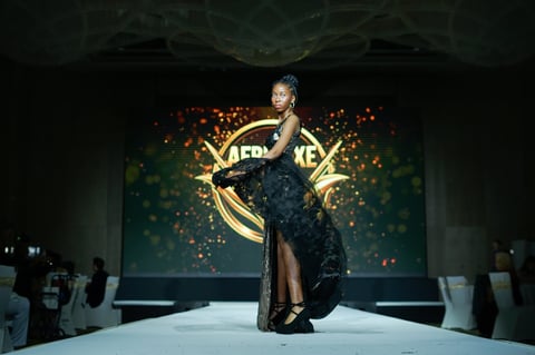 Model walks runway in black sequined gown with gold Los Angeles Lakers logo backdrop during fashion show