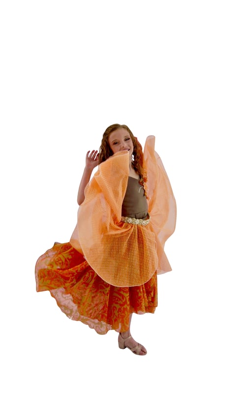 Young girl in colorful dress playfully holding up orange fabric, laughing against white background
