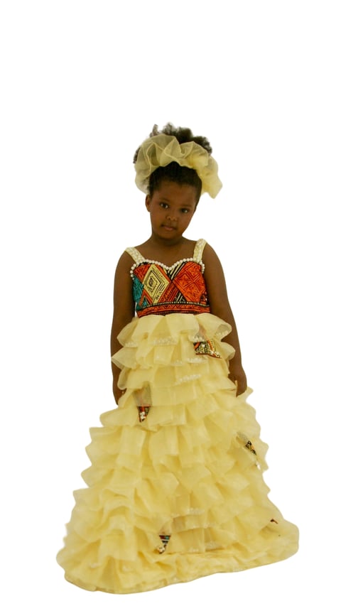 Young child in formal yellow tulle gown with colorful geometric bodice and matching headpiece, standing against white background