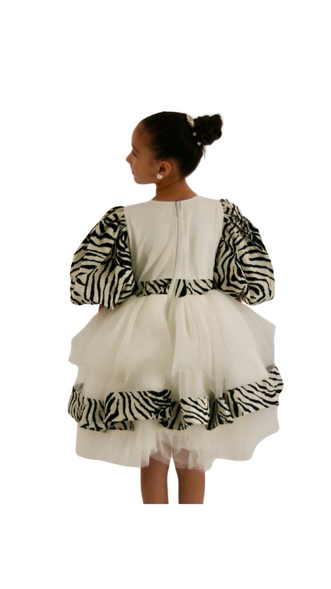 Young girl wearing a cream dress with zebra stripe patterned puff sleeves and ruffled hem, viewed from behind