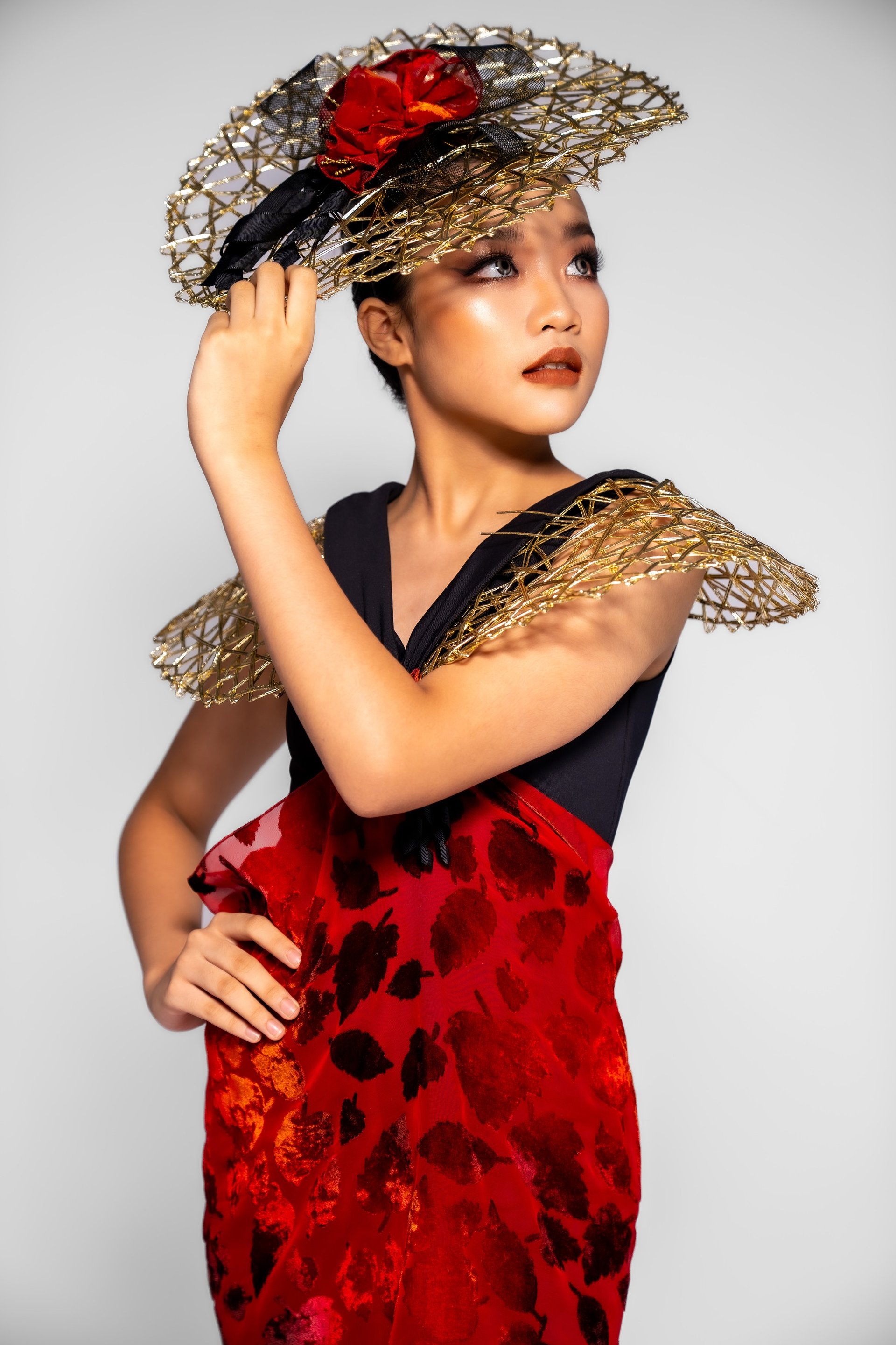 Woman in red leopard print dress with straw hat and gold mesh shoulder pieces, posing against white background