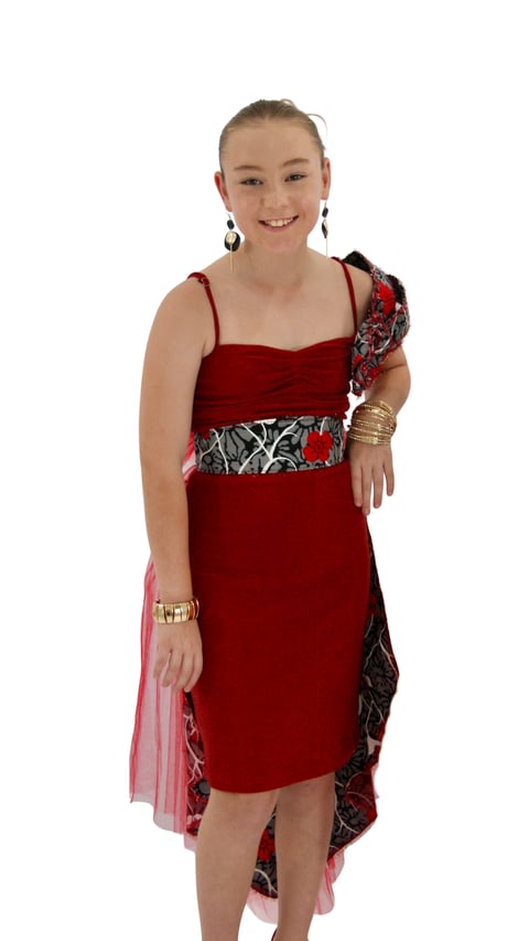 Young girl smiling at camera wearing a red and patterned sleeveless dress with gold bracelets