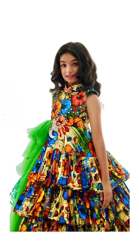 Young girl wearing a vibrant multicolored floral dress with a green tulle bow, posed against a white background