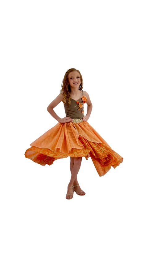 Young girl wearing an orange and brown dress with a twirling skirt, smiling at camera against white background