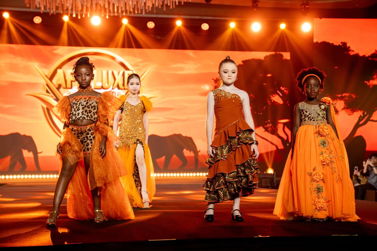 Four young models on stage wearing colorful African-inspired animal print and orange dresses under warm golden stage lighting