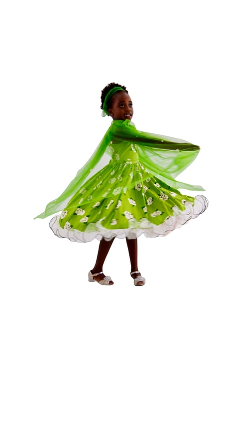 Young child wearing a bright green fairy costume with wings and floral patterns, twirling against a white background