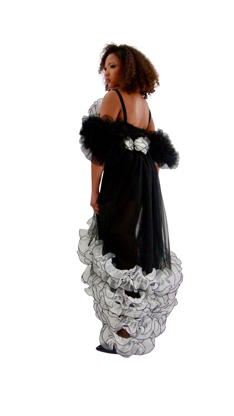 Woman wearing elegant black and white gown with ruffled hem and feathered shoulders, photographed from behind against white background